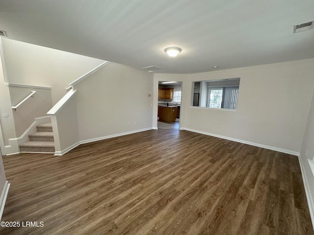 unfurnished living room featuring dark wood-style floors, baseboards, stairs, and visible vents