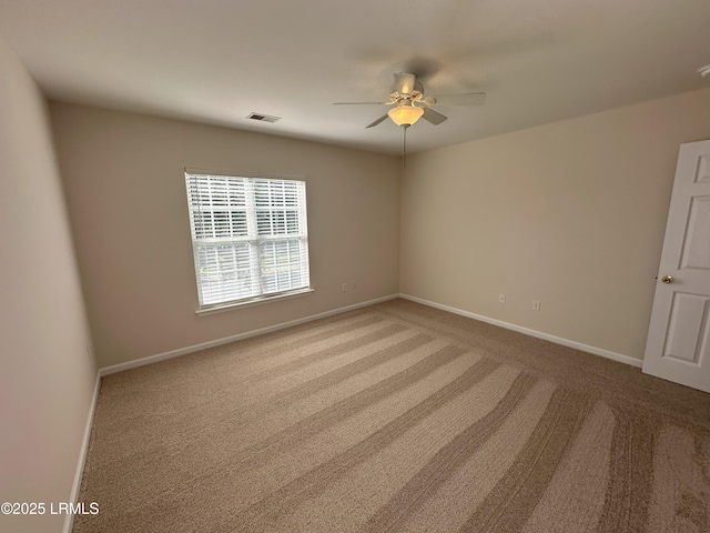 carpeted empty room with a ceiling fan, visible vents, and baseboards