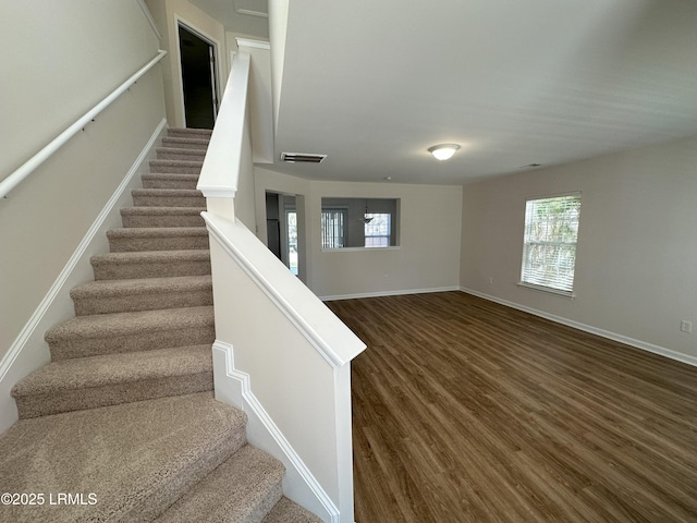 staircase featuring baseboards, wood finished floors, visible vents, and a healthy amount of sunlight