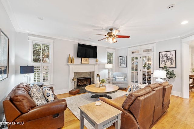 living room with crown molding, light hardwood / wood-style floors, a tile fireplace, and french doors