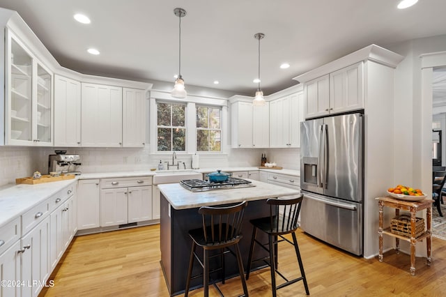 kitchen featuring light hardwood / wood-style flooring, a kitchen island, pendant lighting, stainless steel appliances, and white cabinets