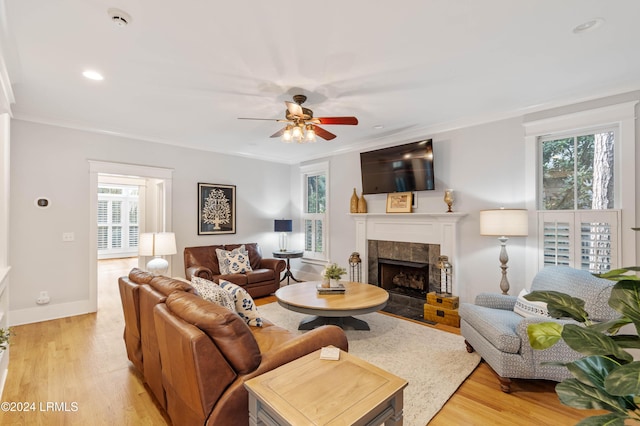 living room with a tiled fireplace, ornamental molding, light hardwood / wood-style floors, and a healthy amount of sunlight