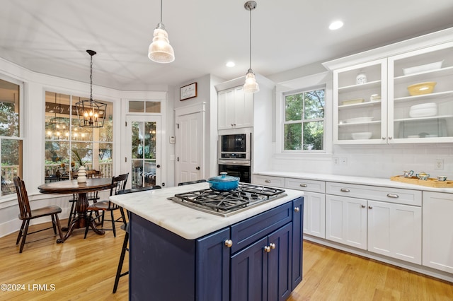 kitchen featuring light hardwood / wood-style flooring, appliances with stainless steel finishes, white cabinetry, hanging light fixtures, and decorative backsplash