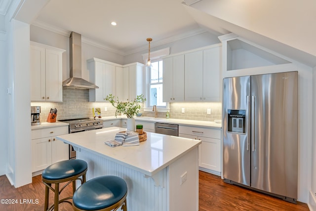 kitchen with wall chimney range hood, appliances with stainless steel finishes, hanging light fixtures, white cabinets, and a kitchen island