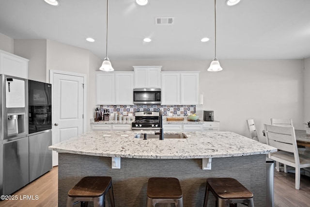 kitchen with stainless steel appliances, white cabinets, and a kitchen island with sink