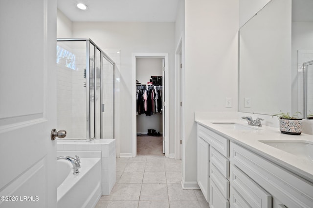 bathroom with a garden tub, double vanity, a spacious closet, a stall shower, and a sink