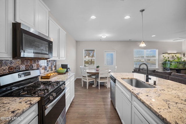 kitchen with decorative light fixtures, backsplash, appliances with stainless steel finishes, white cabinets, and a sink