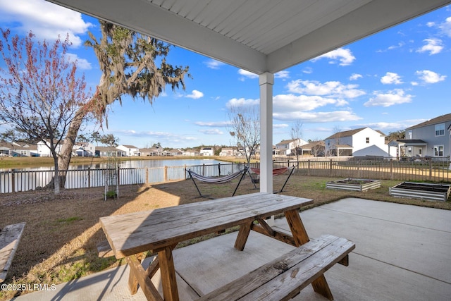 view of patio featuring outdoor dining area, a water view, a fenced backyard, a residential view, and a garden