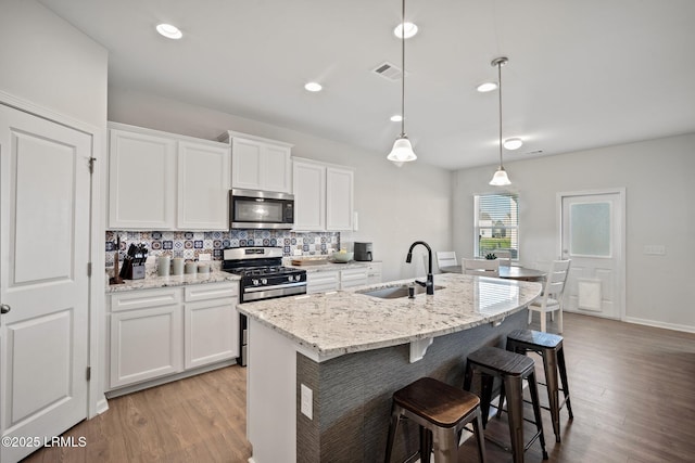 kitchen with white cabinets, stainless steel appliances, a center island with sink, and decorative light fixtures