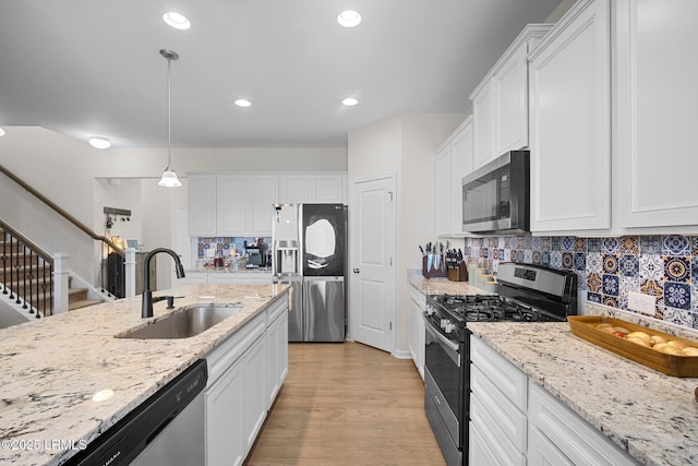 kitchen with stainless steel appliances, decorative light fixtures, a sink, and white cabinetry