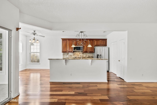 kitchen featuring a breakfast bar area, wood finished floors, stone countertops, appliances with stainless steel finishes, and backsplash