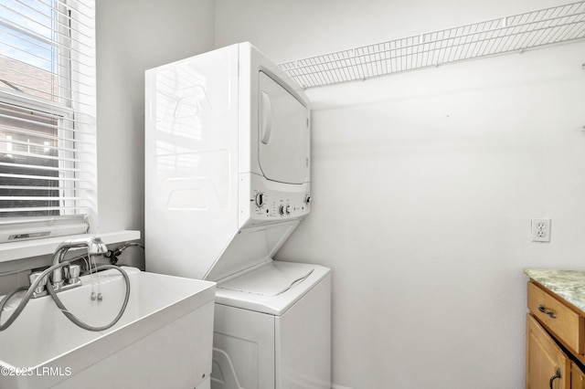 laundry room featuring cabinet space, stacked washer / drying machine, and a sink