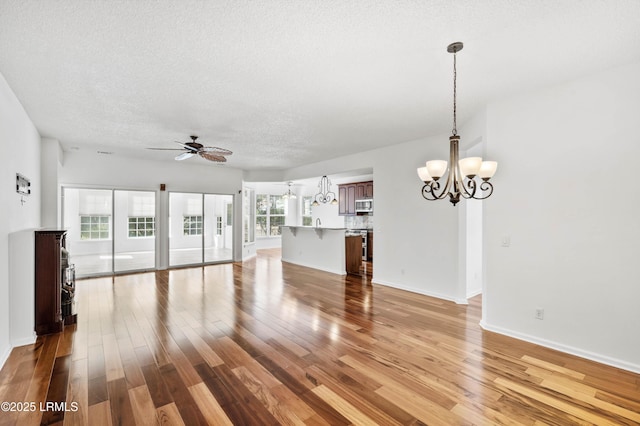 unfurnished living room featuring light wood finished floors, ceiling fan with notable chandelier, a textured ceiling, and baseboards