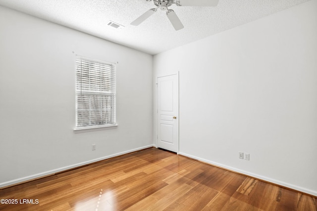 unfurnished room with visible vents, a textured ceiling, wood finished floors, baseboards, and ceiling fan