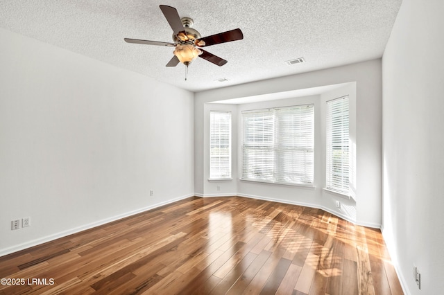 unfurnished room with visible vents, a textured ceiling, baseboards, and wood finished floors