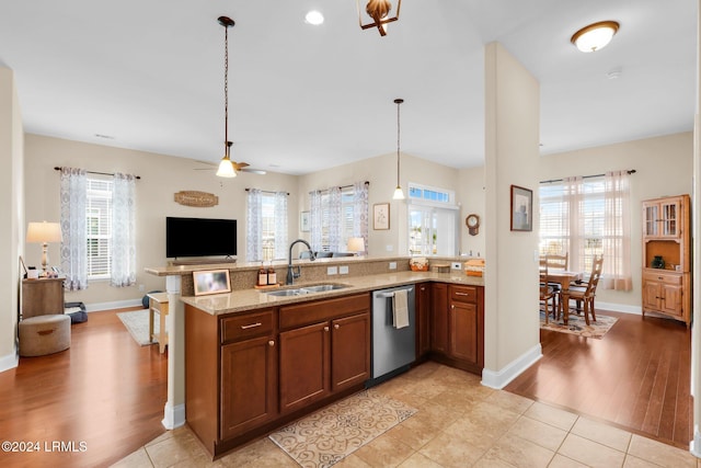 kitchen featuring sink, light tile patterned floors, dishwasher, hanging light fixtures, and light stone counters