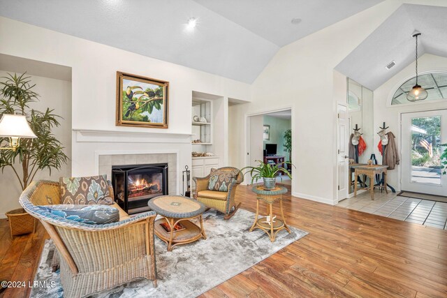 living room featuring a tiled fireplace, lofted ceiling, built in features, and light hardwood / wood-style flooring