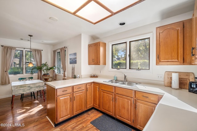 kitchen featuring kitchen peninsula, sink, hanging light fixtures, and light hardwood / wood-style flooring