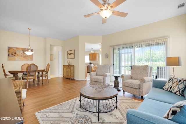 living area with visible vents, a ceiling fan, baseboards, and light wood-type flooring