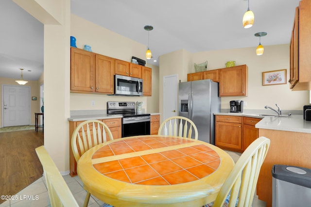 kitchen featuring hanging light fixtures, a sink, light countertops, light tile patterned floors, and stainless steel appliances