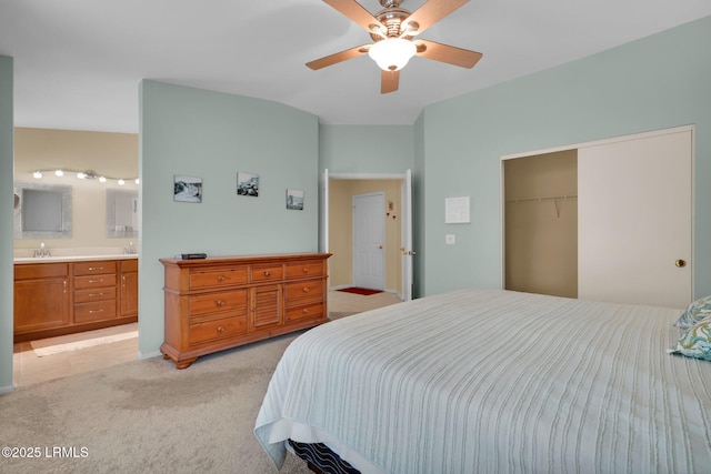bedroom featuring light carpet, a sink, a ceiling fan, ensuite bathroom, and a closet