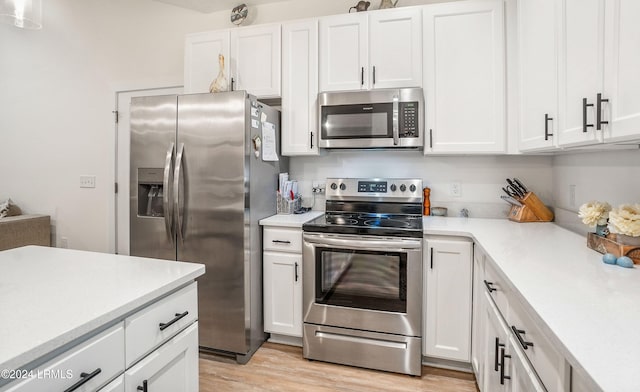 kitchen with stainless steel appliances, white cabinets, and light hardwood / wood-style flooring