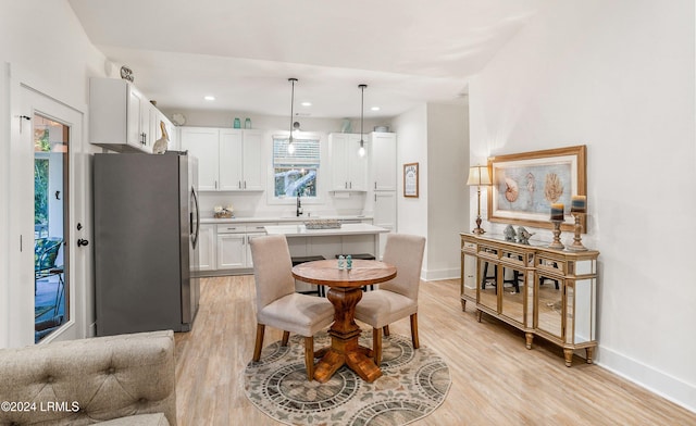 kitchen featuring decorative light fixtures, light hardwood / wood-style flooring, stainless steel refrigerator, and white cabinets