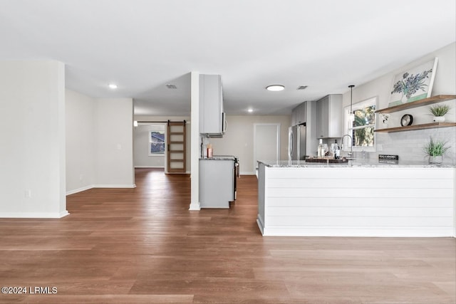 kitchen with stainless steel refrigerator, light stone counters, kitchen peninsula, a barn door, and dark wood-type flooring