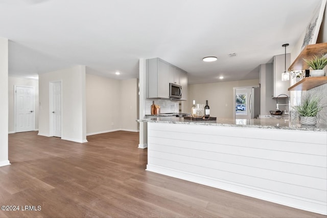 kitchen featuring pendant lighting, appliances with stainless steel finishes, hardwood / wood-style floors, light stone counters, and kitchen peninsula