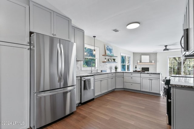 kitchen featuring sink, hardwood / wood-style flooring, appliances with stainless steel finishes, light stone counters, and decorative light fixtures