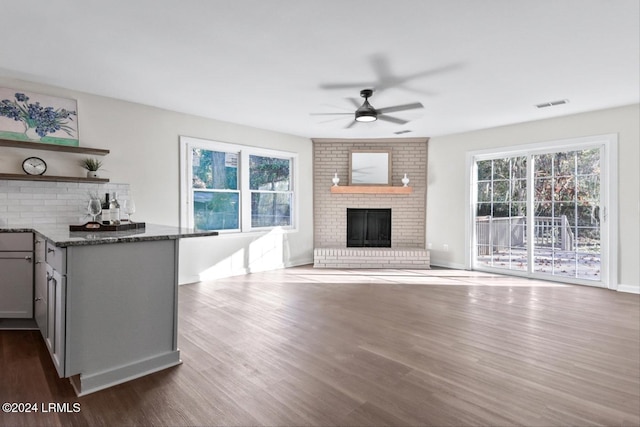 unfurnished living room with ceiling fan, dark hardwood / wood-style flooring, and a brick fireplace