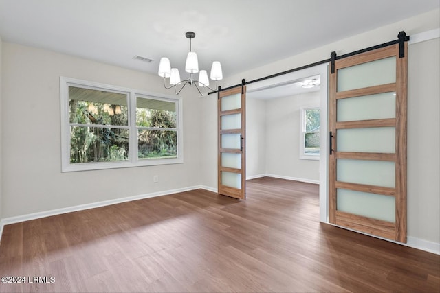 unfurnished room featuring an inviting chandelier, a barn door, and dark wood-type flooring