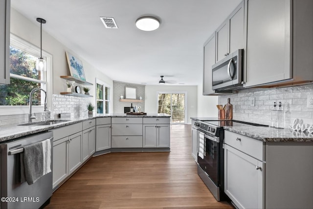 kitchen with pendant lighting, stainless steel appliances, light stone countertops, and sink