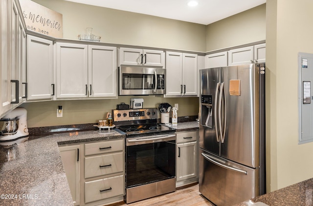 kitchen featuring gray cabinetry, stainless steel appliances, light hardwood / wood-style flooring, and dark stone counters