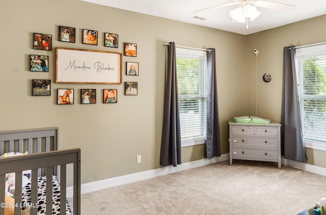 bedroom featuring a nursery area, light carpet, and ceiling fan