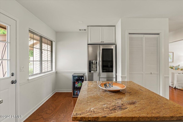 kitchen with dark wood-type flooring, stainless steel refrigerator, wine cooler, light stone countertops, and white cabinets