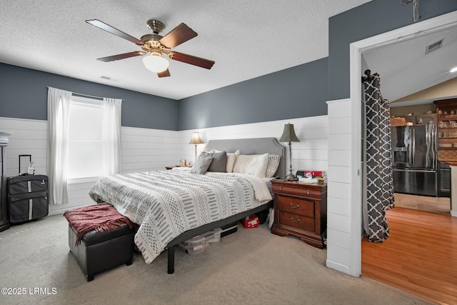 bedroom with ceiling fan, black fridge with ice dispenser, light colored carpet, and a textured ceiling