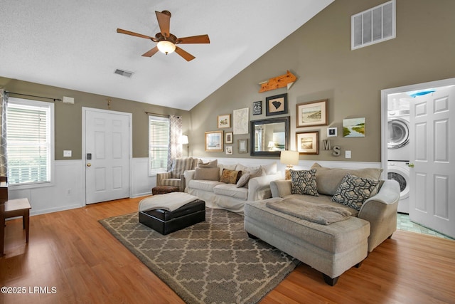 living room featuring stacked washer and dryer, wood-type flooring, high vaulted ceiling, and ceiling fan