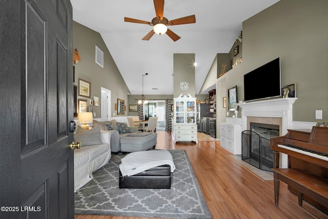 living room featuring ceiling fan, wood-type flooring, a tiled fireplace, and high vaulted ceiling