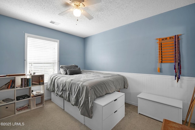 bedroom with light carpet, ceiling fan, and a textured ceiling