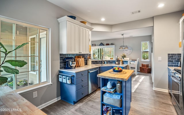 kitchen with appliances with stainless steel finishes, white cabinetry, butcher block counters, a center island, and decorative light fixtures