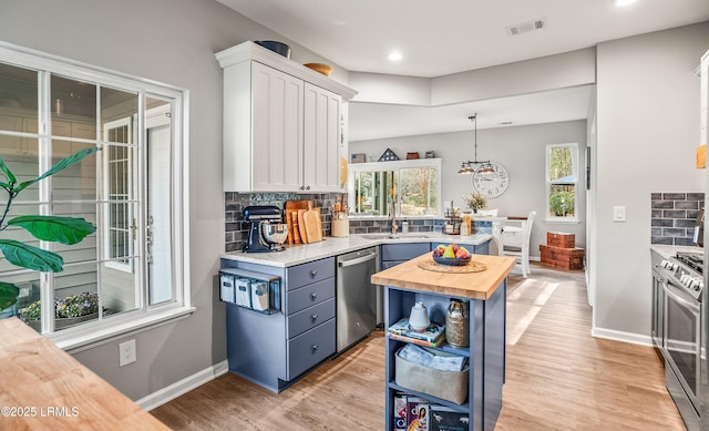 kitchen with a kitchen island, appliances with stainless steel finishes, pendant lighting, butcher block countertops, and white cabinetry