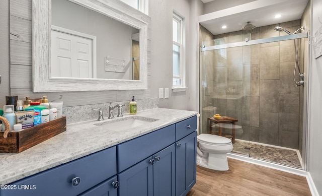 bathroom featuring wood-type flooring, toilet, a shower with shower door, and vanity