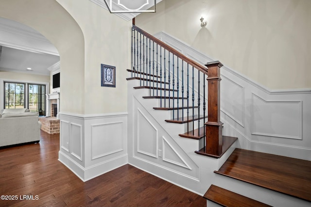 staircase featuring hardwood / wood-style flooring, ornamental molding, and a brick fireplace