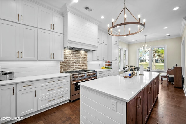 kitchen featuring an inviting chandelier, tasteful backsplash, white cabinets, a center island with sink, and range with two ovens