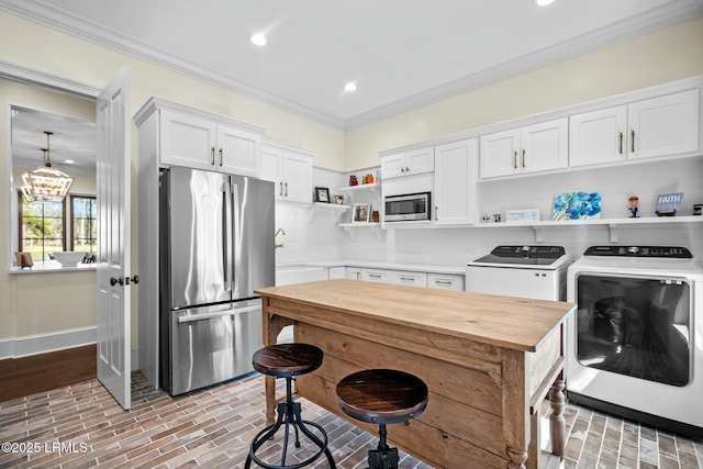 kitchen featuring washing machine and clothes dryer, crown molding, stainless steel appliances, decorative backsplash, and white cabinets