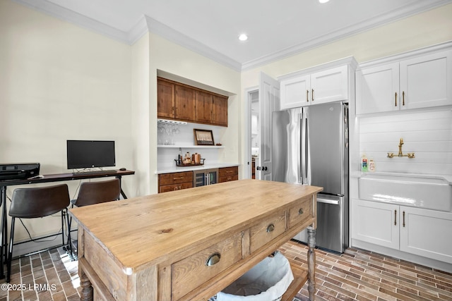 kitchen with ornamental molding, sink, white cabinets, and stainless steel refrigerator