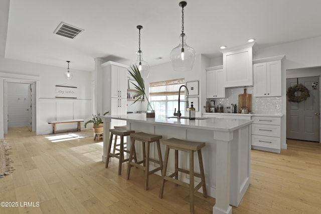 5 Canebrake Ln, Bluffton, SC 29910 - kitchen with backsplash, light countertops, an island with sink, a sink, and white cabinets