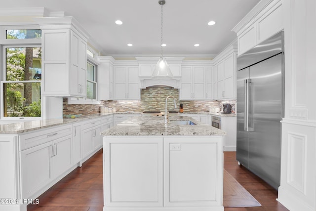 kitchen featuring built in refrigerator, an island with sink, hanging light fixtures, and white cabinets