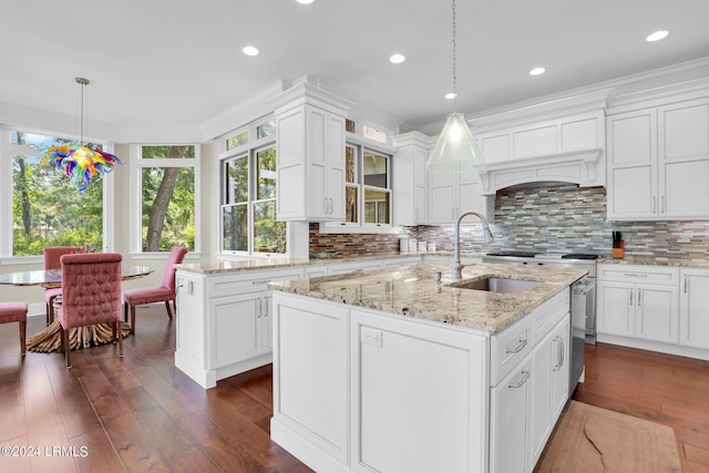 kitchen with sink, white cabinetry, pendant lighting, a kitchen island with sink, and decorative backsplash